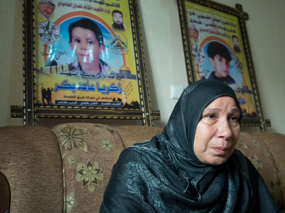 Sharifa Bakr sits in front of posters commemorating Ahed and Zachariah Bakr, photo by Dan Cohen
