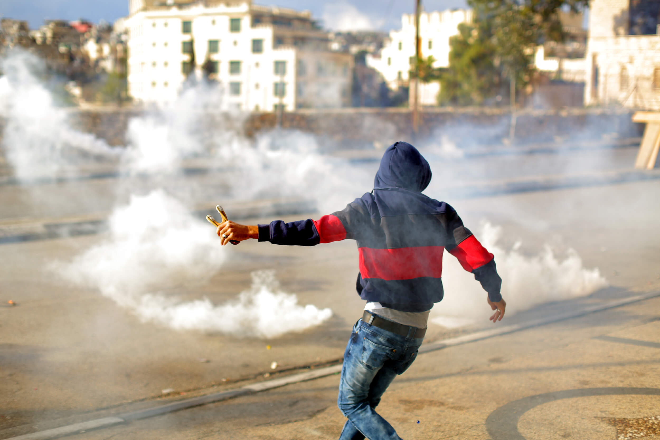 A Young man fires off one last rock from his sling shot before retreating away from the noxious gas. (Photo: Abed al Qaisi)