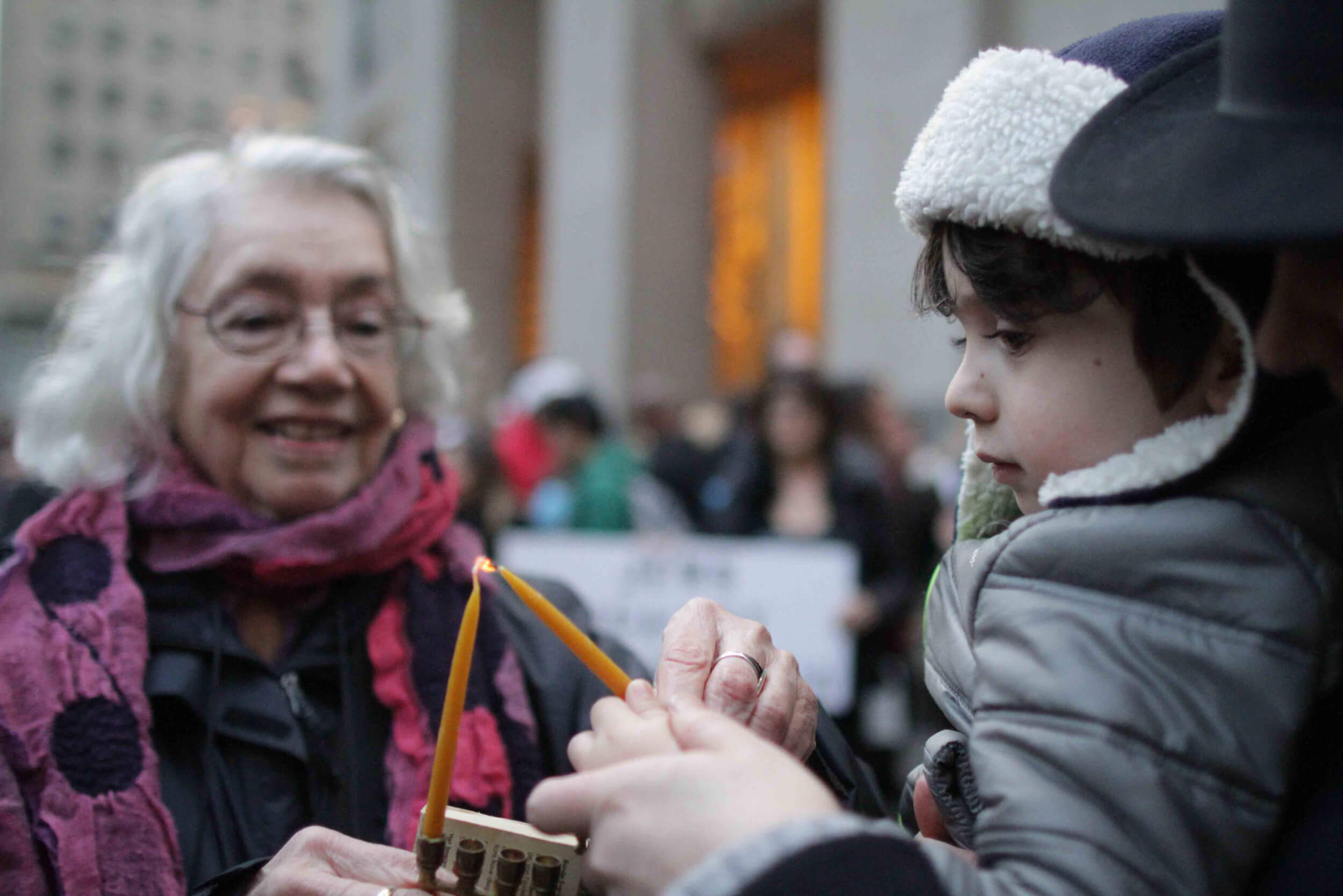 Dorothy Zellner and a young volunteer help light a menorah. (Photo: Jewish Voice for Peace)