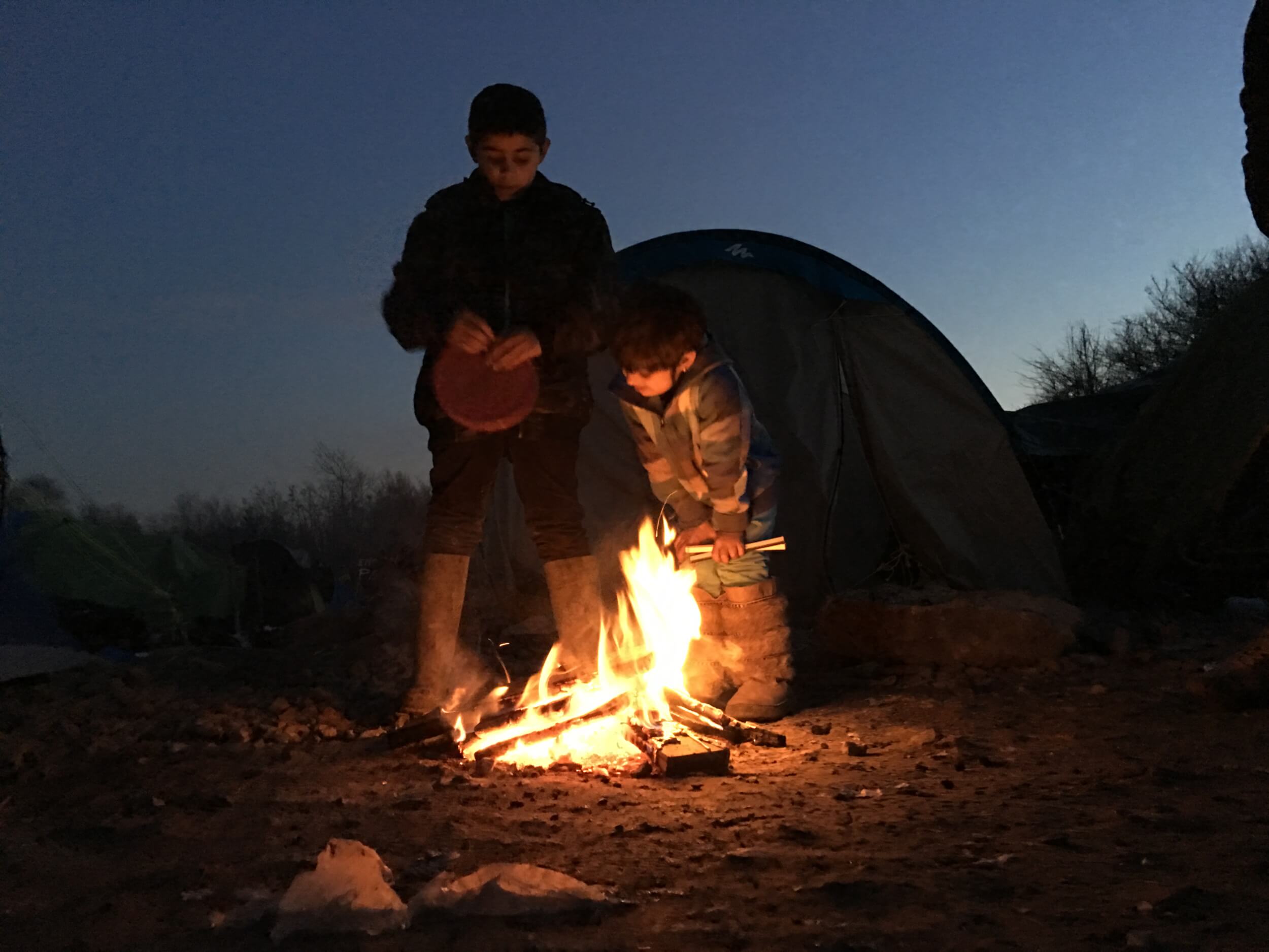 Anas, 10, and Shadi, 6 look on to a fire next to their tent. They have been in Grande-Synthe for eleven days. (Photo: Katherine Schwartz)