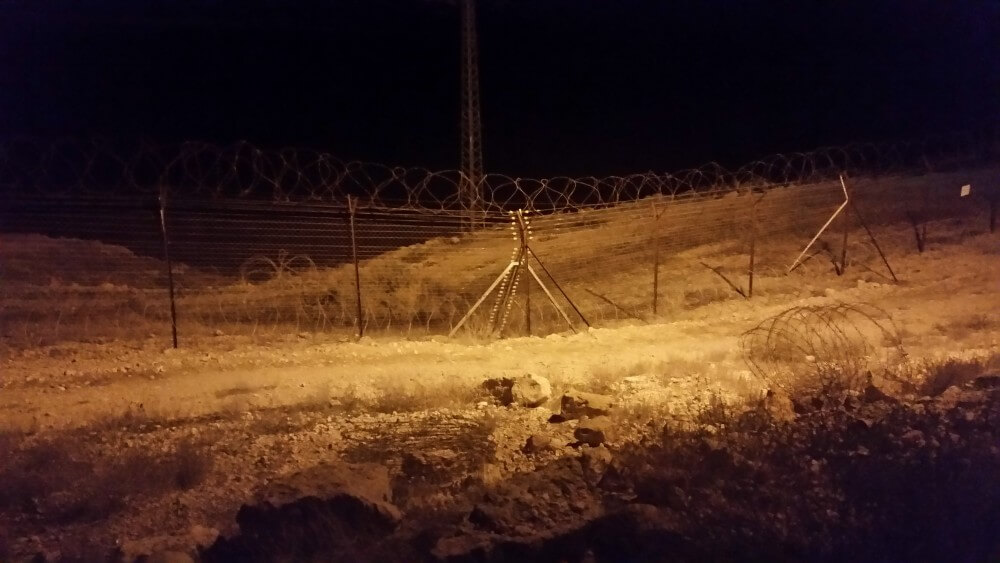 Walking the perimeter of kibbutz Naaran at night. Note the spools of concertina wire behind the similarly-topped fence
