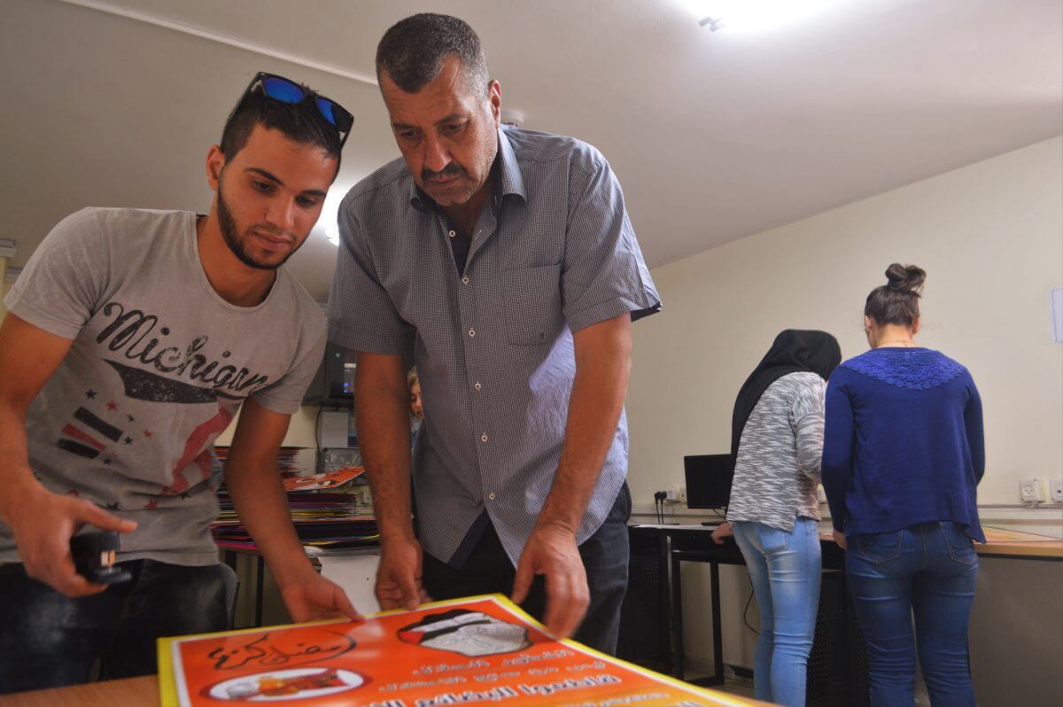 Mazin al-Azzeh helps youth put together stacks of BDS campaign posters. (Photo: Sheren Khalel/Mondoweiss)