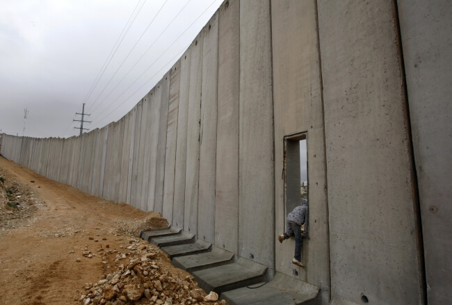 Palestinian boy climbs through an opening in Israel's separation barrier in Shuafat near Jerusalem. February, 2009. (Photo: REUTERS/Baz Ratner)
