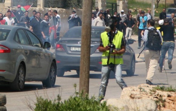 Mohammad working as a volunteer photographer for B'tselem, wearing his gas mask and press jacket and carrying his camera. 