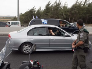 An Israeli policeman walks by cars with Israeli flags while carrying a confiscated Palestinian flag. (Photo: Dan Cohen)