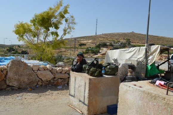 IDF soldier talks on her phone while cars wait to exit Hebron at a new Area A entrance checkpoint. (Photo: Sheren Khalel)