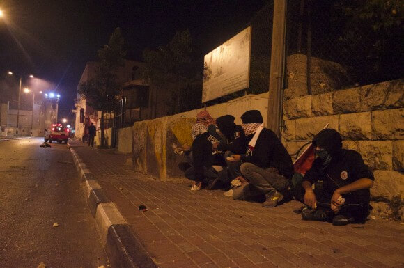 Young men take cover behind cement blocks while holding rocks at the ready. (Photo: Sheren Khalel)