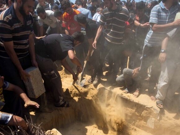 Mourners shovel and push dirt by hand into a grave. (Photo: Dan Cohen)