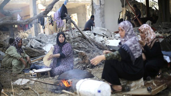 14 August 2014. Palestinian women bake bread in front of the remains of their house in Khan Younis, in the southern Gaza Strip. (Photo: Reuters/I. Abu Mustafa via ICRC)