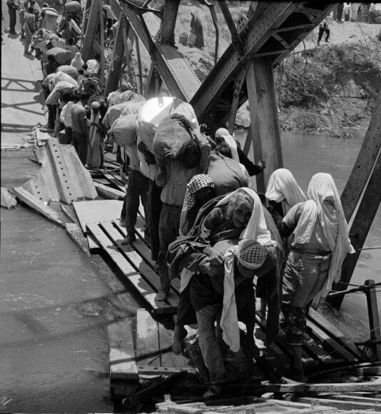 In this 1967 photo from the U.N. Relief and Works Agency, UNRWA, archive, Palestine refugees flee across over the Jordan river on the damaged Allenby Bridge during the 1967 Arab-Israeli war. 