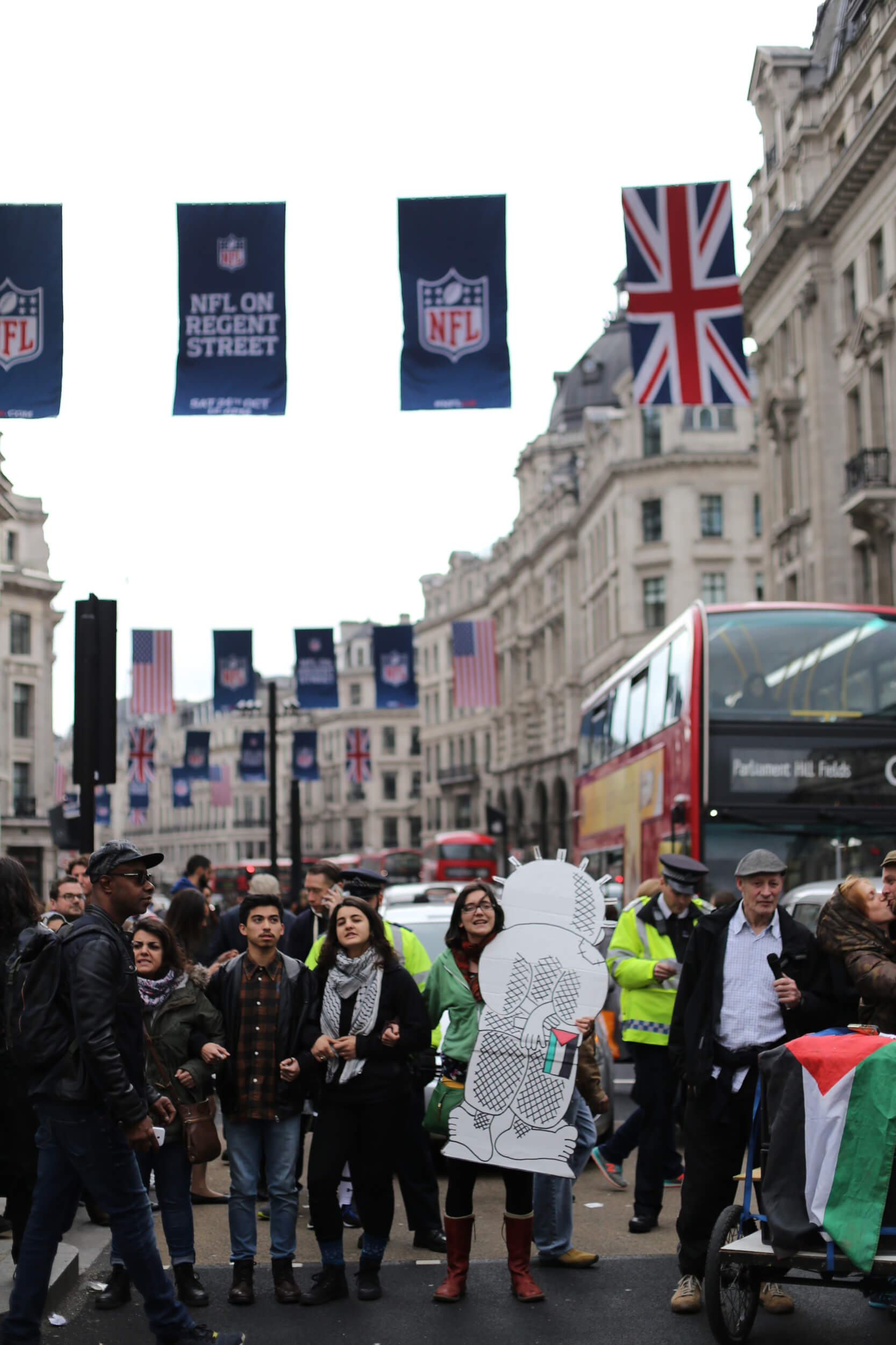 Protesters link arms stopping traffic on Oxford Street. Some hold representations of Handala, a creation of the late Palestinian cartoonist Nagi Al-Ali. Handala bears witness to the Israeli oppression of the Palestinian people. (Photo: Sara Anna)
