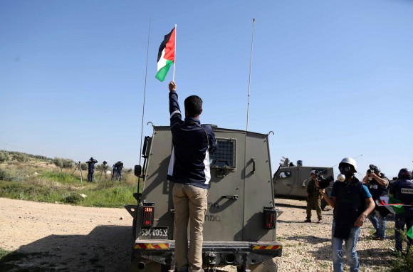 A Palestinian man puts a national flag atop a vehicle of Israeli security forces during clashes following a march on February 19, 2016 in the West Bank village of Bilin, near Ramallah, to mark the 11th anniversary of their uprising against the building of Israel's controversial separation barrier and the construction of Israel settlements. (Photo: Shadi Hatem/ APA Images)