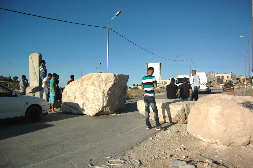Palestinians wait for rides near roadblocks erected by the Israeli military in the West Bank town of Yatta. (Photo: Allison Deger) 