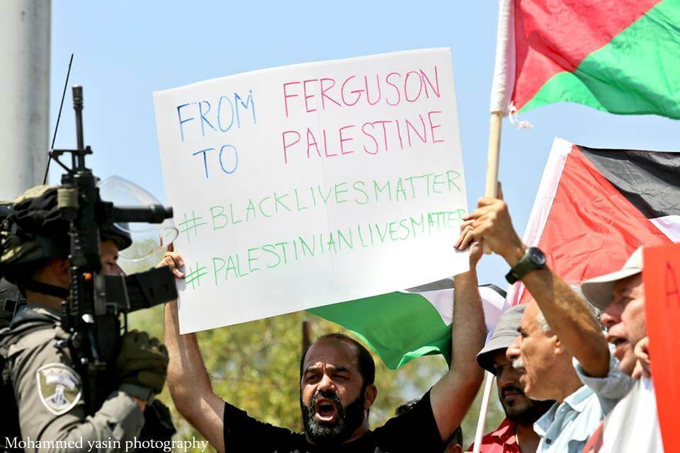 Munther Amira carries a Palestinian flag and a poster reading "From Ferguson to Palestine, #BlackLivesMatter, #PalestinianLivesMatter" during a 2016 protest in the occupied West Bank. (Photo courtesy of Munther Amira)