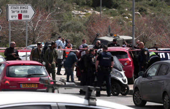 Members of the Israeli Israeli security forces stand guard next to a car at the site of an attack at the Ariel junction