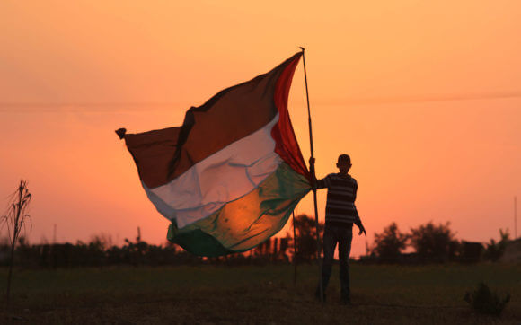Un uomo palestinese sventola una bandiera della Palestina prima dell'inizio delle proteste della Grande Marcia del Ritorno il 29 marzo 2018. (Foto: Ashraf Amra/APA Images)