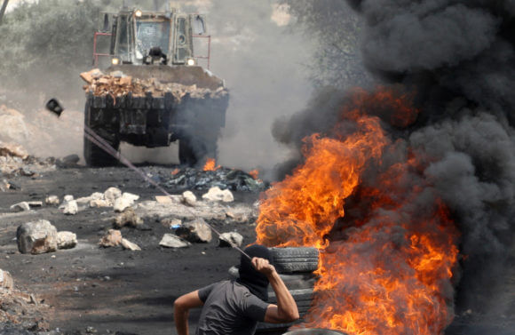 A Palestinian protester uses a slingshot to throw stones towards an Israeli military truck