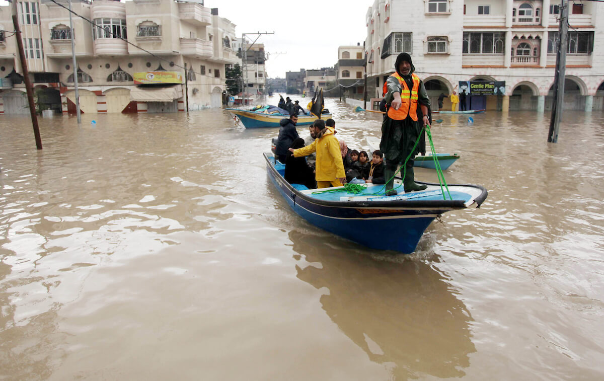 Palestinian civil defense volunteers help people to travel across flood waters in Gaza City following rain storms, on December 14, 2013. A fierce winter storm shut down much of the Middle East at that time, burying Jerusalem in snow, and flooding parts of Gaza. (Photo: Ashraf Amra/APA Images)