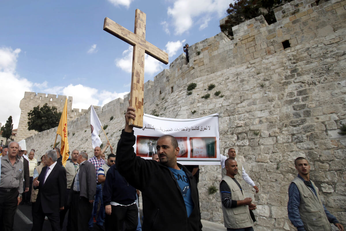 A Palestinian protester holds a cross during a demonstration against acts of vandalism on Christian sites including smashing headstones in a Christian cemetery in Israel and the occupied West Bank, outside Jerusalem's Old City October 6, 2013. (Photo: Saeed Qaq/APA Images)