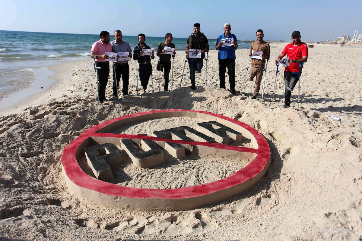 Palestinian amputees who were injured by Israeli forces stand in front a sand castle in a protest calling to boycott sportswear retailer Puma, on the beach of Gaza City on May 29, 2019. Puma is the main sponsor of the Israel Football Association (IFA), which includes teams in Israeli settlements. (Photo: Mahmoud Ajjour/APA Images)