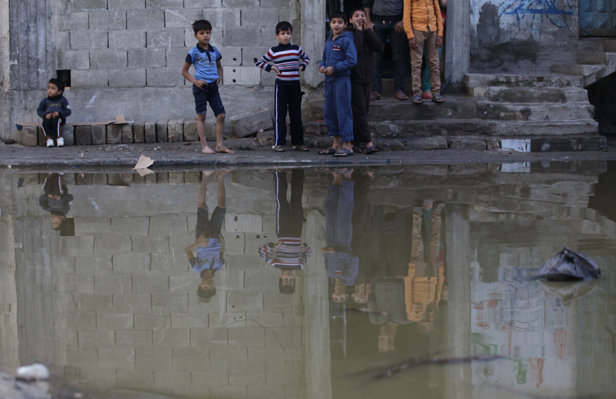 Palestinians look at a flooded street with sewage in al-Sabra neighborhood, in Gaza City on November 13, 2013. The main pump of sewage water which serves thousands of citizens in a densely populated area was stopped during the power cuts in the area due to a fuel shortage, causing sewage overflow out of the station in the lower nearby areas. (Photo: Ashraf Amra/APA Images)
