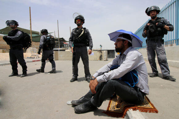 A Palestinian man sits in front of Israeli forces at the Qalandiya military checkpoint, May, 2019.