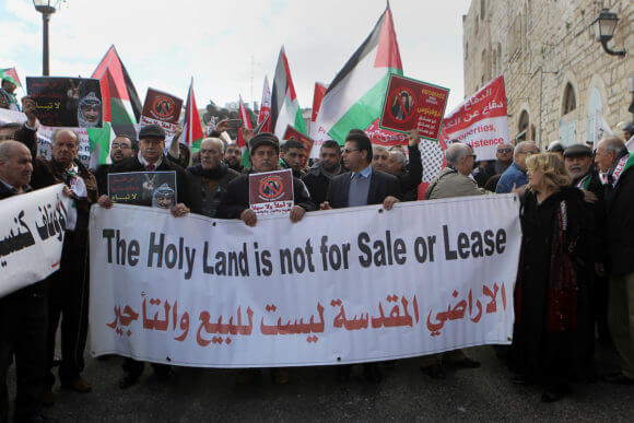 Palestinian protesters hold placards as the convoy of Jerusalem's Greek Orthodox patriarch Theophilos III arrives in the West Bank town of Bethlehem on January 6, 2018 ahead of a Christmas service according to the Eastern Orthodox calendar. The municipalities of Bethlehem, Beit Sahour and Beit Jala, all in the West Bank, called for the boycott over Jerusalem's Greek Orthodox patriarch allegedly allowing controversial real estate sales. (Photo: Wisam Hashlamoun/APA Images)