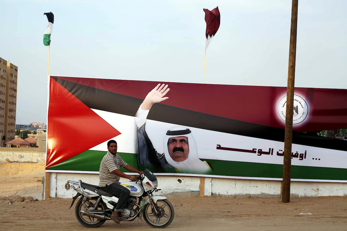 A Palestinian man rides his motorcycle in front of the image of the Emir of Qatar, Sheikh Hamad bin Khalifa Al-Thani, adorn's a barrier where a project funded by Qatar is under construction, in Gaza City on October 21, 2012. (Photo: Ashraf Amra/APA Images)
