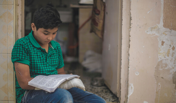 Samer looks at old homework in his own handwriting that he had completed before his injury, in his home in Jabalia refugee camp in the northern Gaza Strip, on May 26, 2019. (Photo: DCIP/Mohammad Ibrahim )