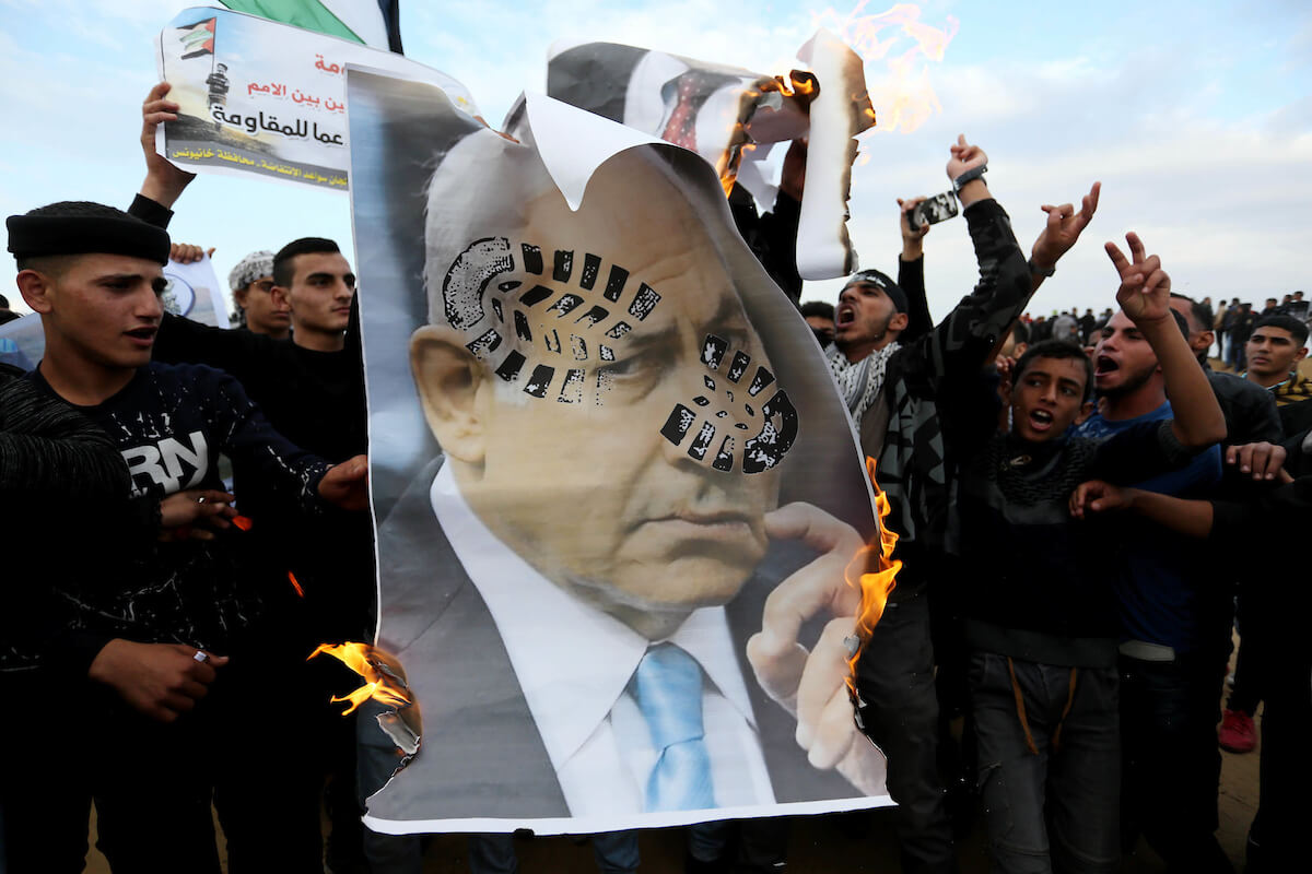 Palestinian protesters deface posters depicting Israeli Prime Minister Benjamin Netanyahu during a protest near the Israel-Gaza border, in Khan Younis in the southern Gaza Strip on November 16, 2018. (Photo: Ashraf Amra/APA Images)