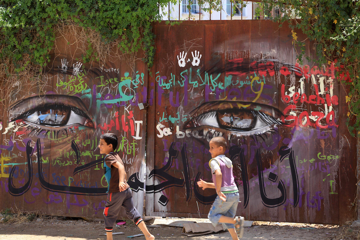 Palestinian children play in front of a gate painted with a mural by the German artist Akot on the walls of houses destroyed during the 2014 war in the Gaza Strip, Gaza City on June 11, 2015. (Photo: Mohammed Asad/APA Images)