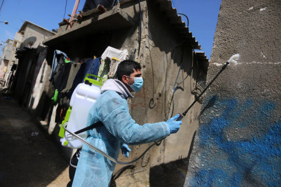 A Palestinian worker wearing protective gear disinfects streets as a preventive measure amid fears of the spread of the coronavirus, at al-Shati refugee camp in Gaza City on March 16, 2020. (Photo: Ashraf Amra/APA)