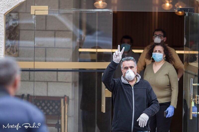 A Palestinian man holds up a peace sign after being released from quarantine in the Angel Hotel. 17 COVID-19 patients from Bethlehem were announced to be in recovery on Friday, March 20th, 15 days after the outbreak in the city began. (Photo: Mustafa Bader, Facebook)