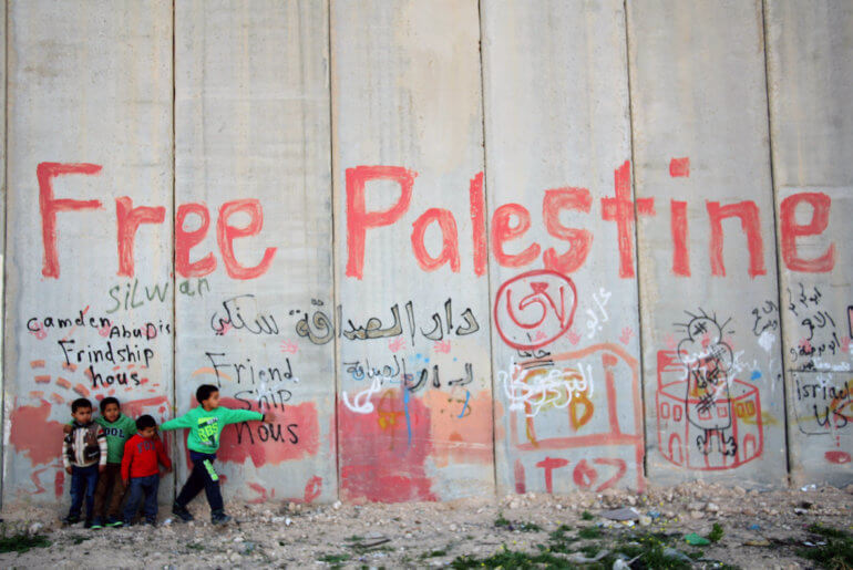 Palestinian children stand in front of Israeli separation barrier in the east Jerusalem village of Abu Dis, April 3, 2014. (Photo: Saeed Qaq/APA Images)