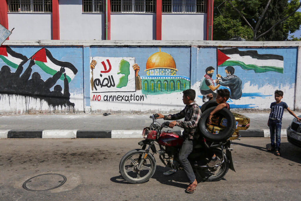 Palestinians ride past a mural protesting Israel's West Bank annexation plans, in Rafah in the southern Gaza Strip, on July 1, 2020. (Photo: Ashraf Amra/APA Images)