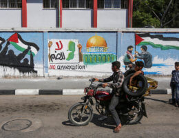 Palestinians ride past a mural protesting Israel's West Bank annexation plans, in Rafah in the southern Gaza Strip, on July 1, 2020. (Photo: Ashraf Amra/APA Images)