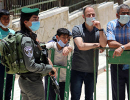 A member of the Israeli security forces stands guard as Palestinians wearing face masks enter the Ibrahimi mosque, to perform the Friday prayer, in the midst of the coronavirus COVID-19 outbreak, in the West Bank town of Hebron on June 26, 2020. (Photo: Mosab Shawer/APA Images)