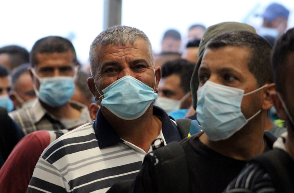 Palestinian laborers wearing masks queue to enter Israel through the Mitar checkpoint in the West Bank city of Hebron on June 28, 2020. (Photo: Mosab Shawer/APA Images)