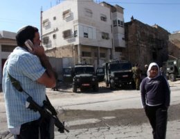 A Palestinian boy and an armed Jewish settler last Thursday outside the guarded building that settlers occupied in the divided West Bank city of Hebron. (Photo: Abed Hashlamoun / EPA)