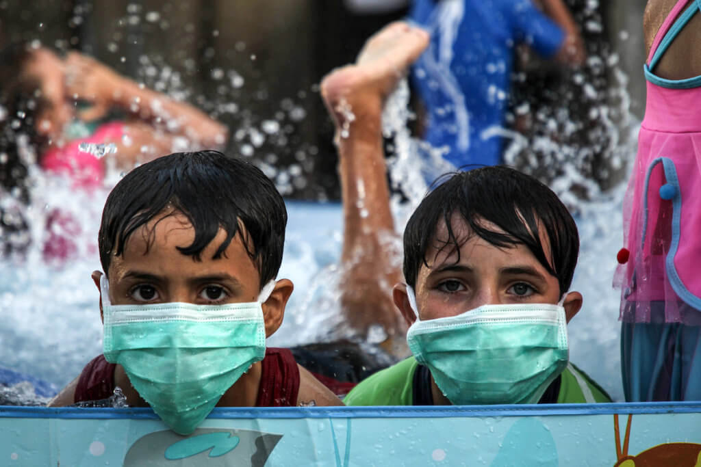 Palestinian children wearing face masks cool off by playing in a pool in Gaza City on September 28, 2020. (Photo: Mahmoud Ajjour/APA Image)