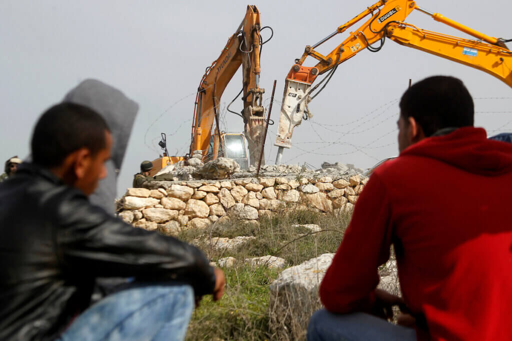 File Photo: Palestinian men watch the demolition of a Palestinian house at the order of the Israeli army in the West Bank village of Beit Ula, west of Hebron January 21, 2016. The owners of the house said they were informed by the Israeli army that the demolition was carried out because they did not have an Israeli-issued construction permit. (Photo: Wisam Hashlamoun/APA Images)