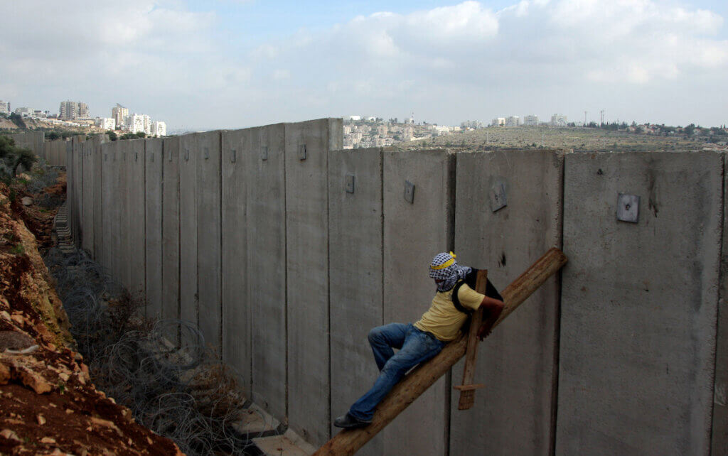 Un manifestante palestinese si arrampica sul muro dell'apartheid israeliano durante una protesta nel villaggio di Nilin in Cisgiordania, venerdì 1 gennaio 2010. (Foto: Issam Rimawi/APA Images)