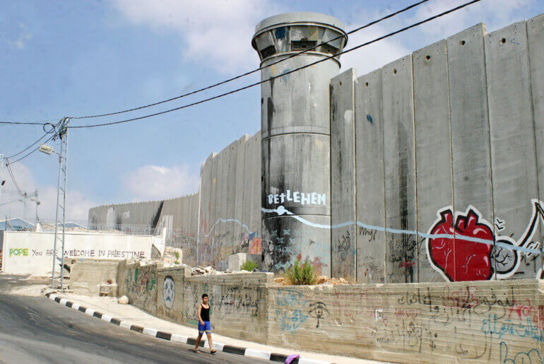 Palestinian children walk beside the Israeli apartheid wall in Aida refugee camp in the West Bank town of Bethlehem on July 6 2009. (Photo: Najeh Hashlamoun/APA Images)