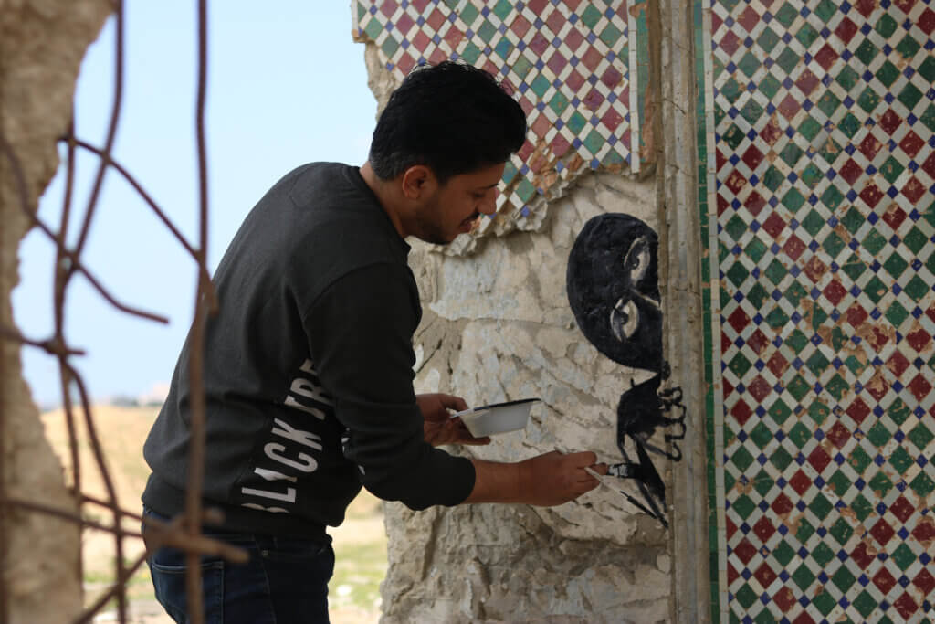 An artist painting on an exposed wall in the destruction. (Photo: Aseel Kabariti)