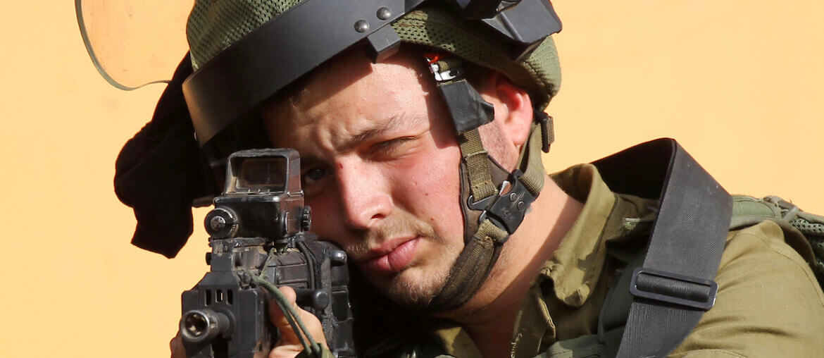 An Israeli soldier aims his weapon towards Palestinian protesters in the West Bank city of Hebron on October 19, 2018. (Photo: Wisam Hashlamoun/APA Images)