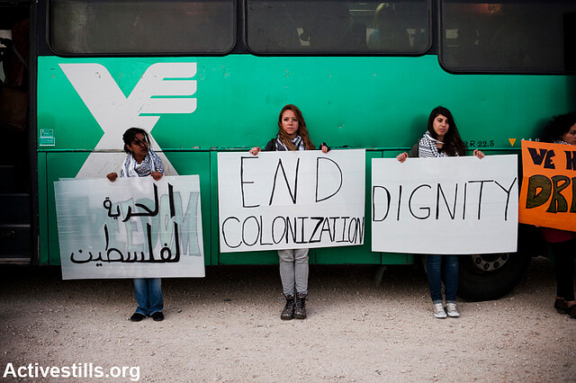 Protesters hold signs outside a bus in the West Bank. (Photo: Activestills)