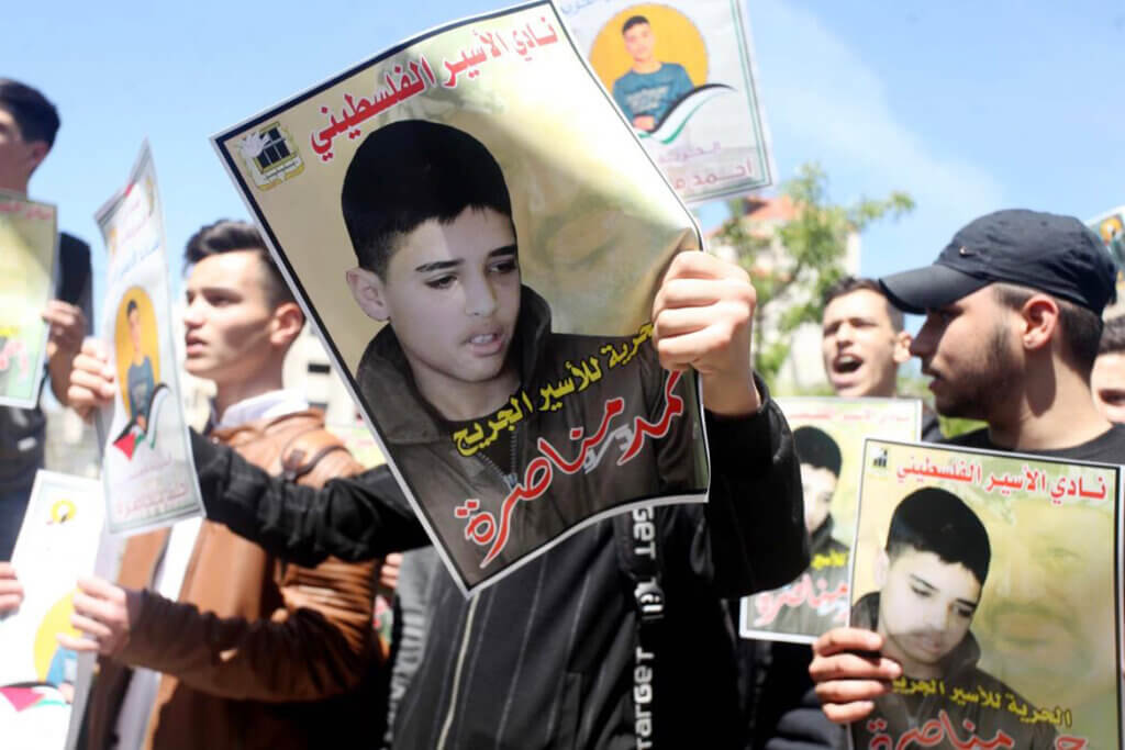 Palestinians hold placards during a protest in solidarity with prisoner Ahmed Manasra, in front of Red Cross office in the West Bank city of Hebron on April 13, 2022. (Photo by Samar Bader/WAFA)