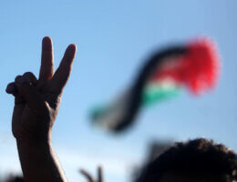 A Palestinian protester holds the victory sign in front of a Palestinian flag, December 2, 2012. (Photo by Issam Rimawi/APA Images)