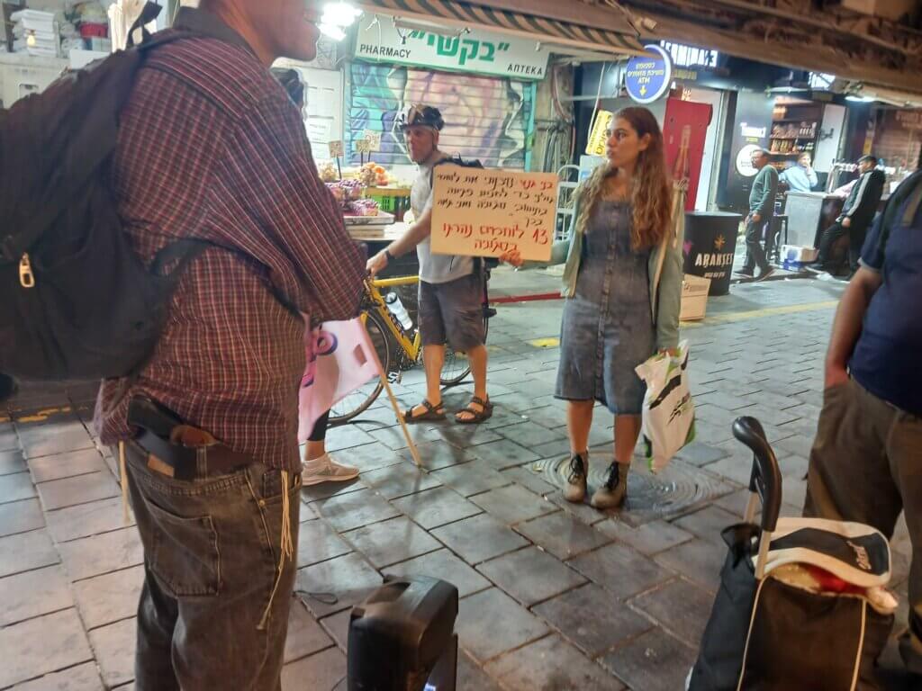 A man with a gun tucked in his belt leads a chant for Netanyahu at Mahane Yehuda market in West Jerusalem. The woman with him, also supporting Netanyahu, holds a sign that says "Gantz has put our soldiers' lives at risk several times. Vote for Netanyahu" (Photo: Philip Weiss)
