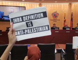 An activist holds up a sign at a Montgomery County Council meeting on October 25 protesting the council's consideration to adopt the IHRA definition of antisemitism. (Photo: Maryland 2 Palestine/Twitter)